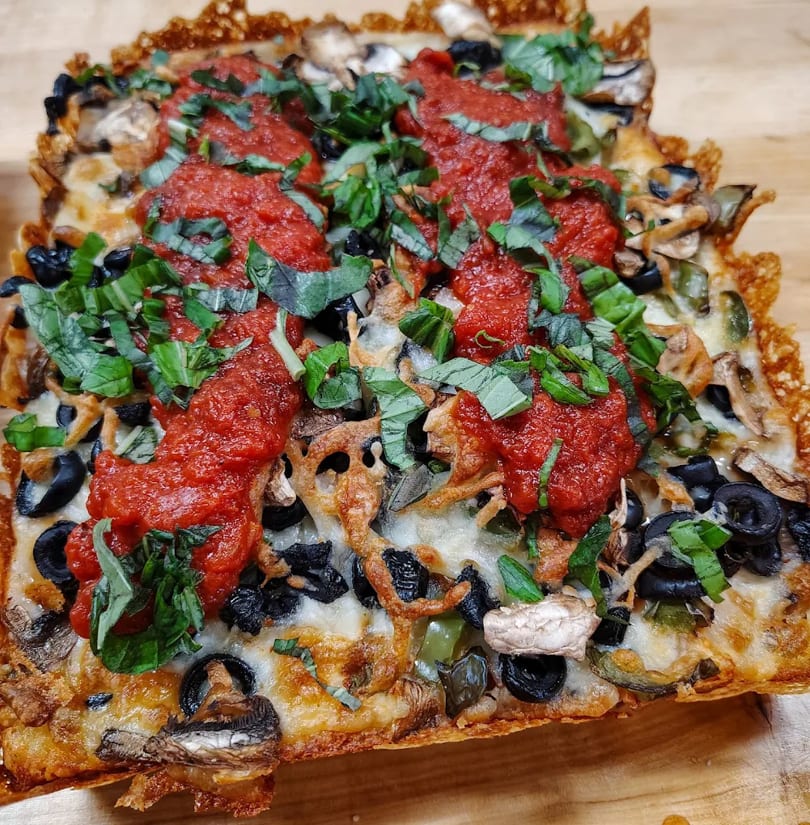Square deep-dish pizza with melted cheese, black olives, mushrooms, green peppers, tomato sauce, and basil.